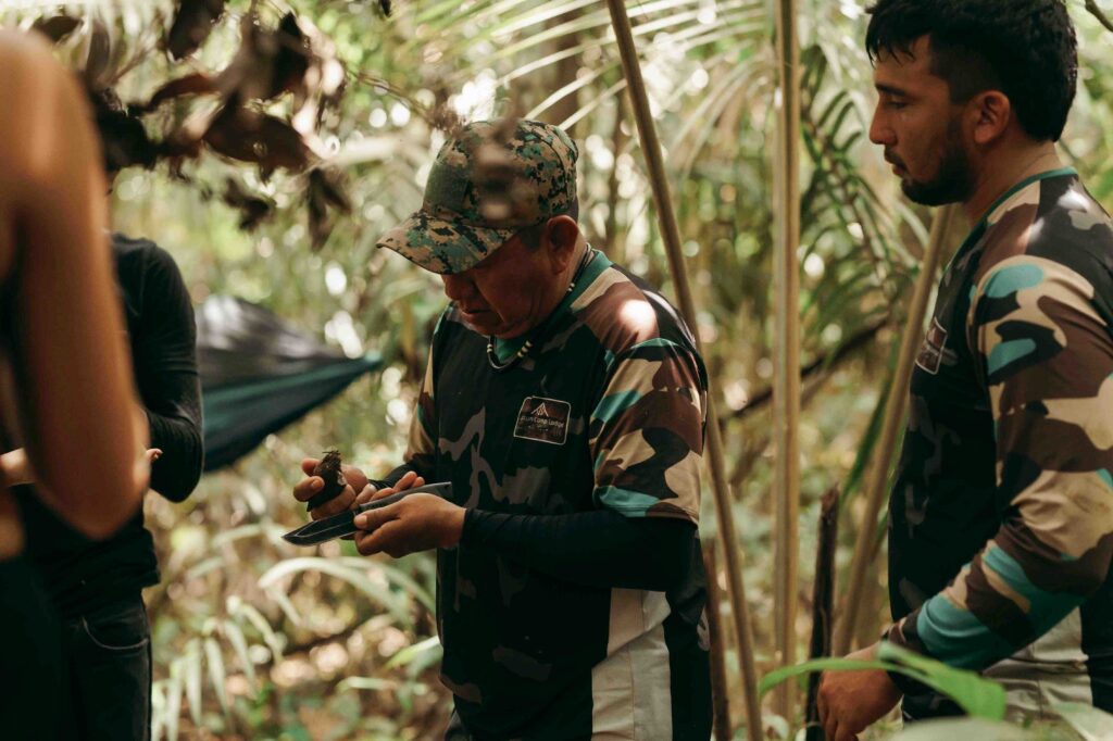 na foto o guia mathias apresenta aos viajantes como identificar frutos comestíveis, ele segura um fruto nas mãos e explica sobre técnicas de sobrevivência na selva
